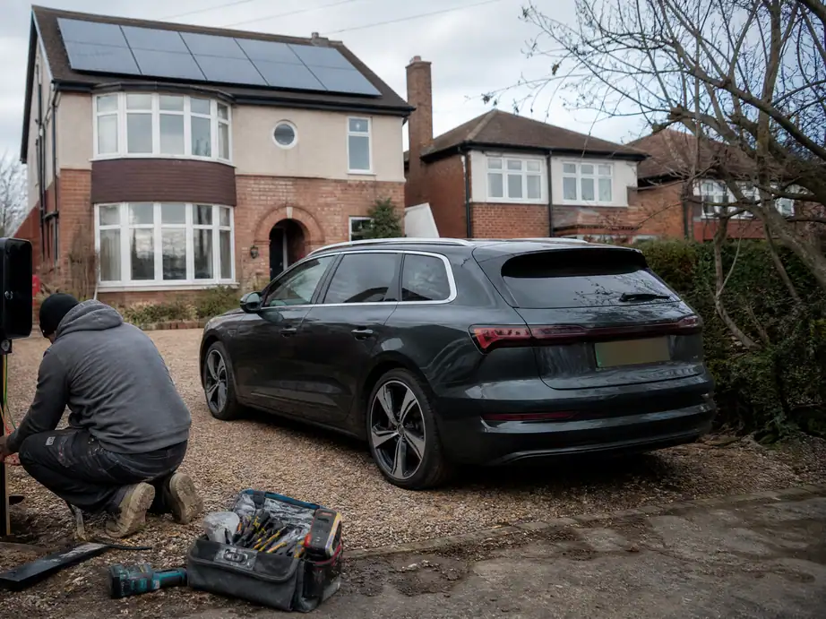 Electrician installing an EV charger on a post beside a gravel drive in Derby